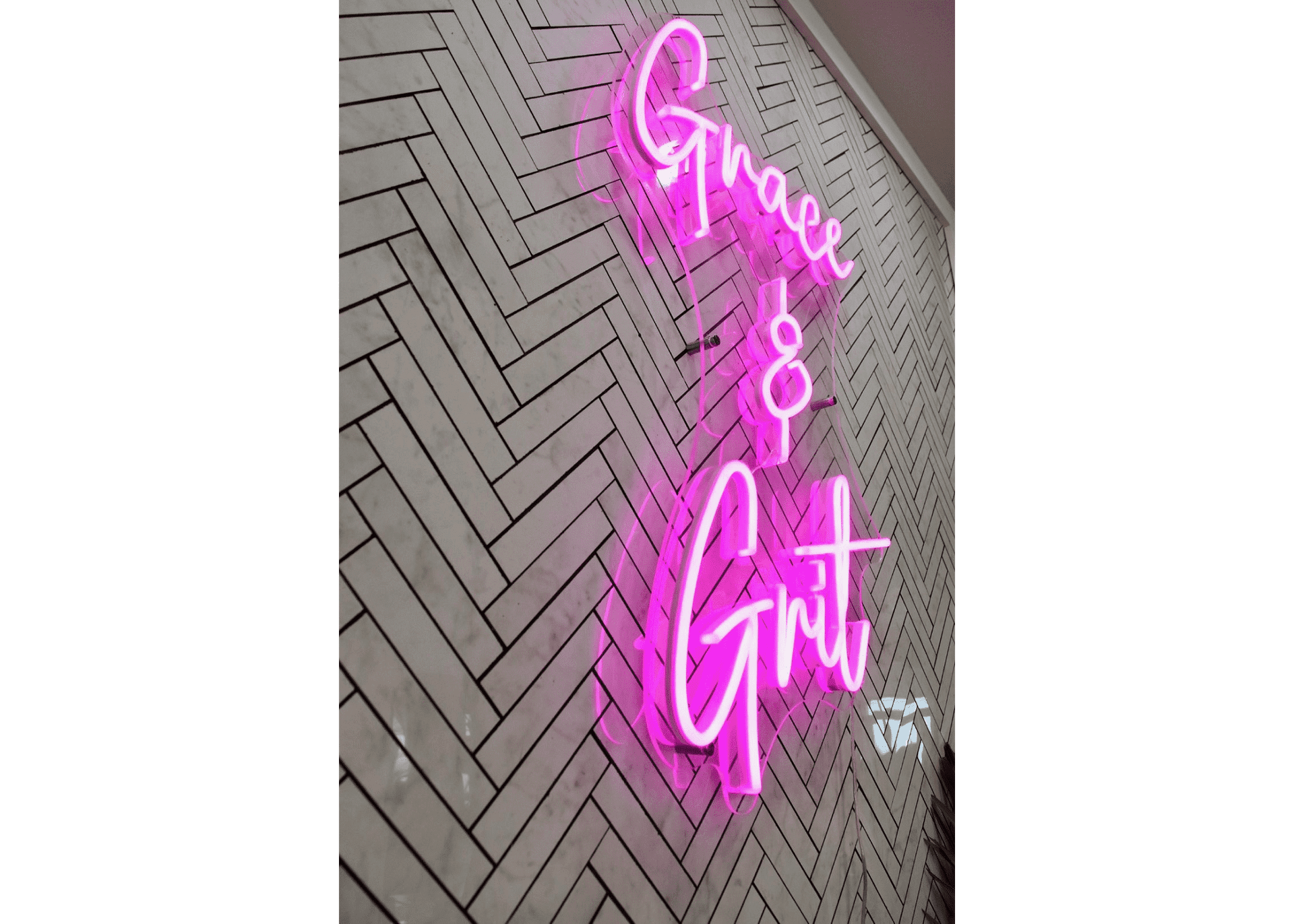 Neon sign reading "Grace & Grit" on a herringbone brick wall background.